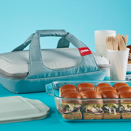 Pyrex baking dish with sandwiches and a carrying case on a blue background