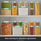 Snapware® clear plastic storage containers with mint green lids stacked on pantry shelves, organizing dry foods including peas, oats, rice, cereal, pasta, nuts, beans, herbs, and spices.
