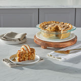 Apple pie with a slice served on a plate with ice cream, placed on a marble countertop.