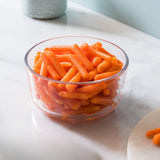 Clear glass bowl filled with orange carrot-like snacks on a light surface.