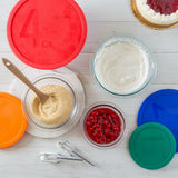 Bowls of ingredients with colorful lids on a white surface
